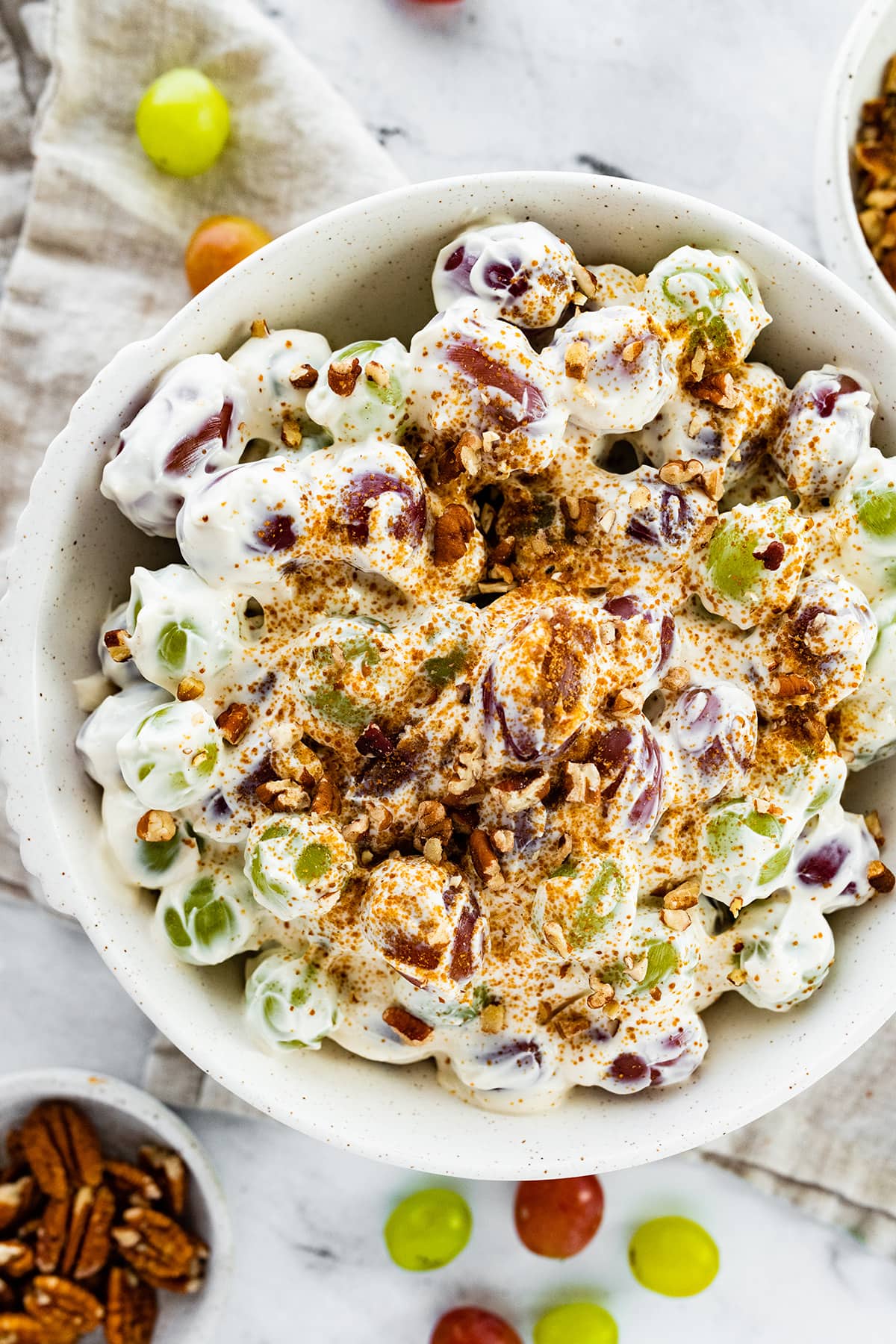 Creamy grape salad topped with sugar and crushed pecans in a large bowl.