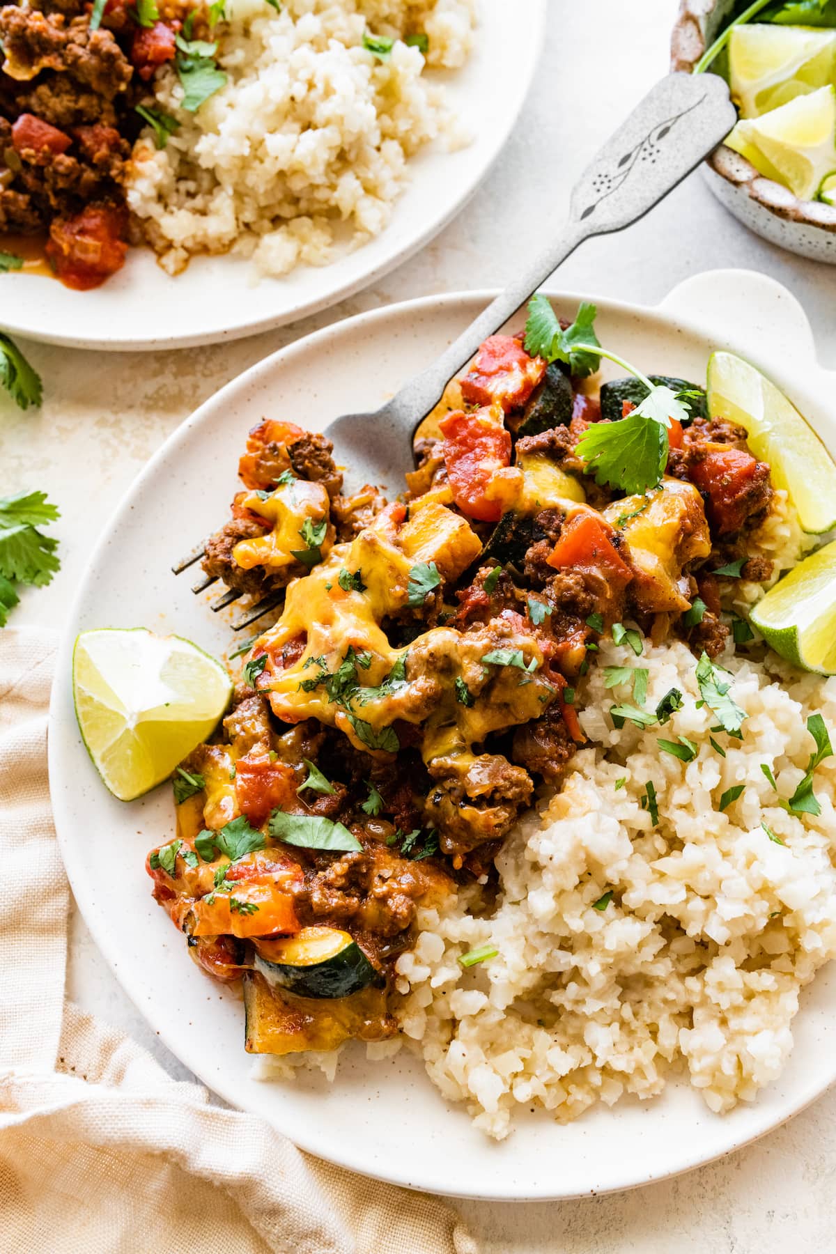 A serving of ground beef and squash skillet recipe on a plate with a side of brown rice and lime slices.