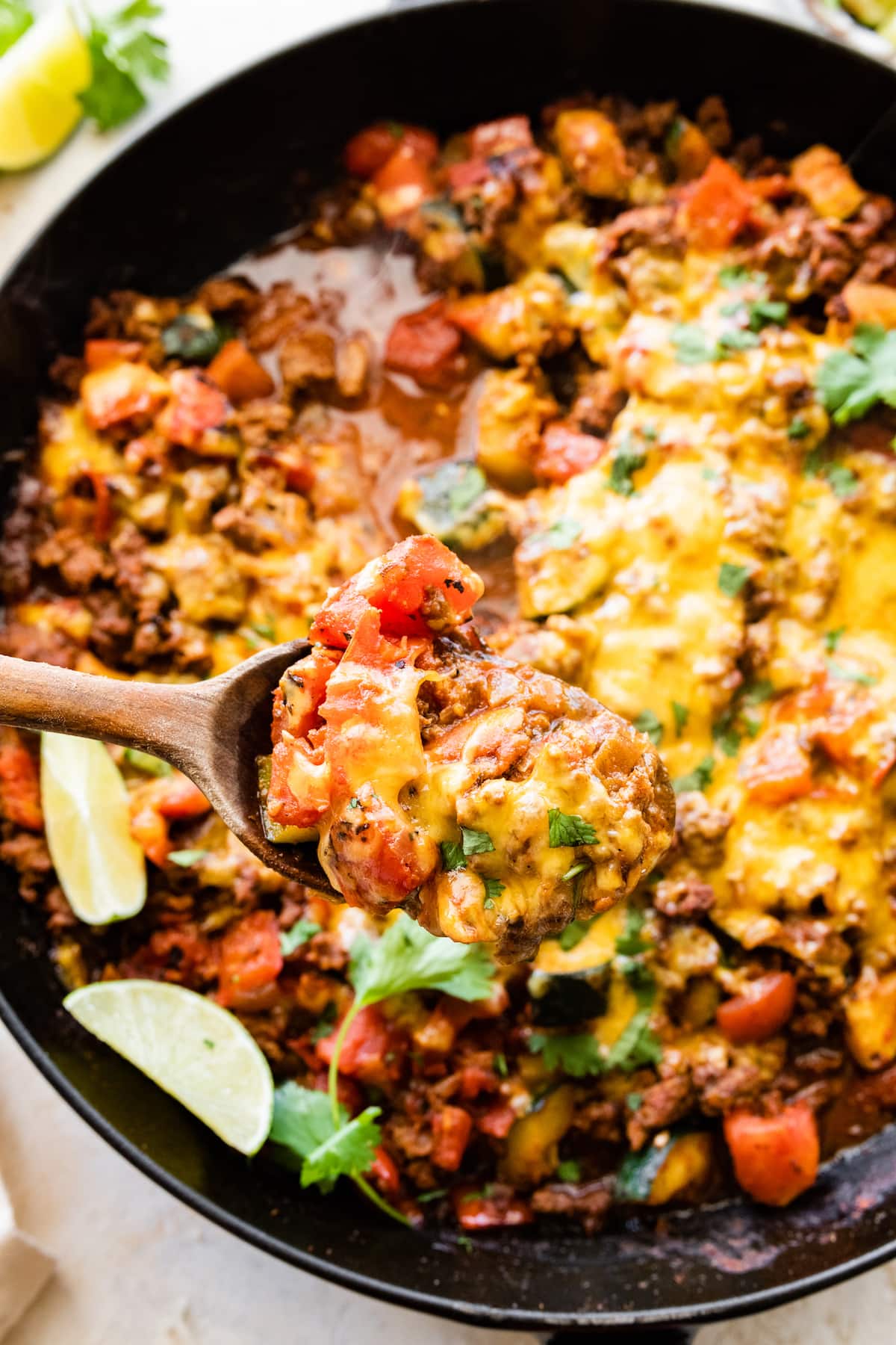 A wooden serving spoon holding a spoonful of ground beef and squash over a skillet.