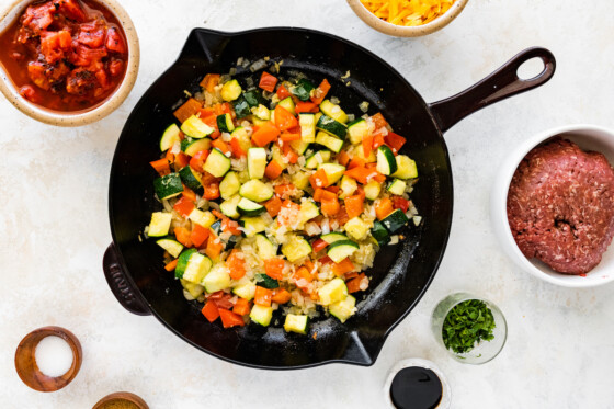 Diced zucchini and bell pepper in a large cast iron skillet with onion and garlic.