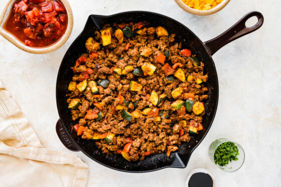 Ground beef cooked in a large cast iron skillet with zucchini, red bell pepper, onion, and garlic.