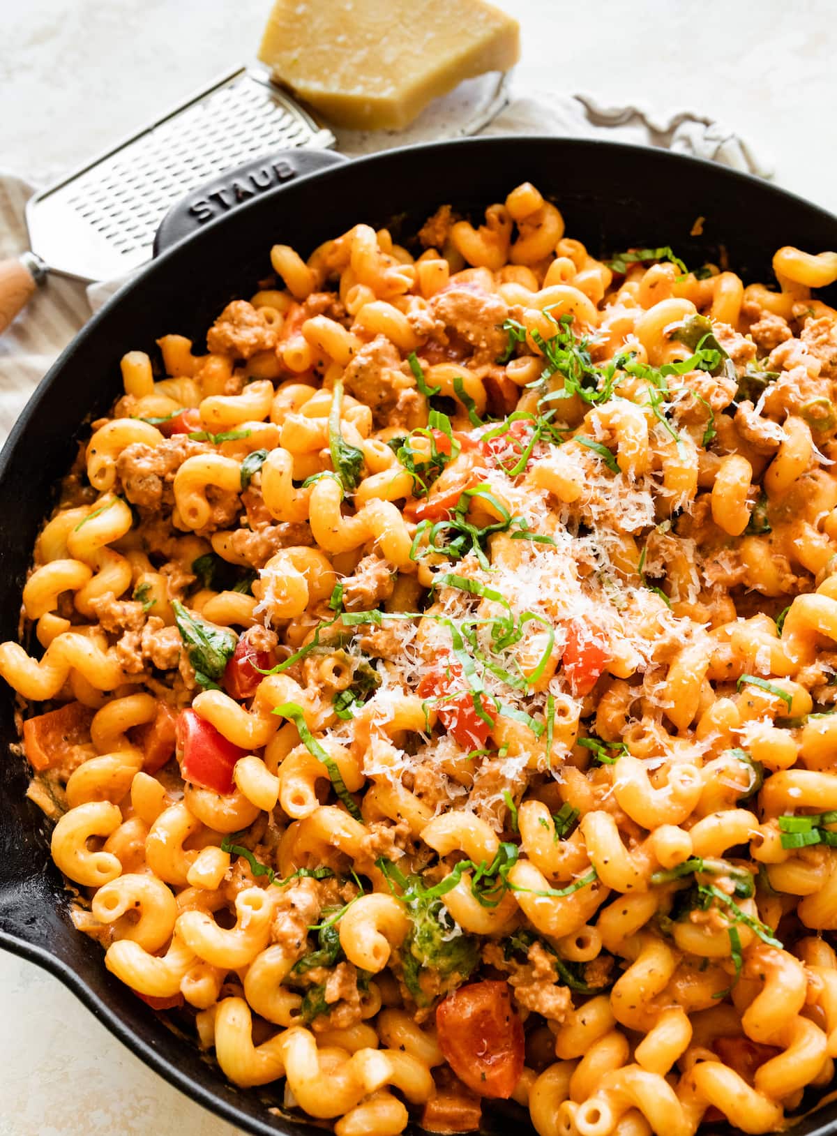 A large cast iron skillet with ground turkey pasta garnished with parmesan cheese.