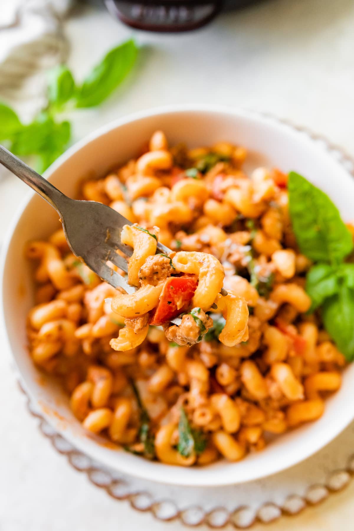 A fork holding a bite size serving of ground turkey pasta over a bowl of the pasta.