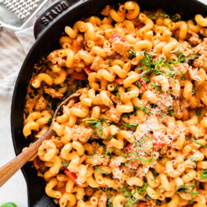 A large cast iron skillet with ground turkey pasta garnished with parmesan cheese. There's a wooden serving spoon in the skillet.