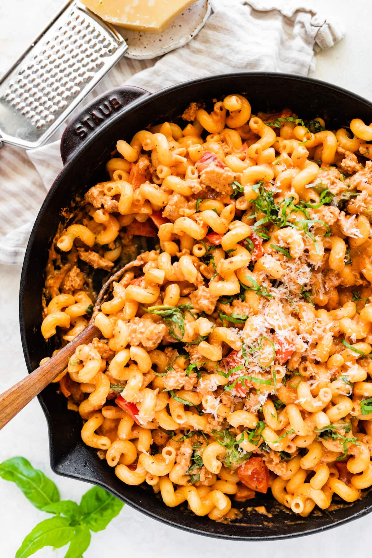 A large cast iron skillet with ground turkey pasta garnished with parmesan cheese. There's a wooden serving spoon in the skillet.