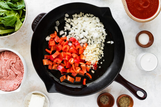 Diced red bell pepper, garlic, and onion in a cast iron skillet.