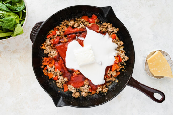 Cream cheese and tomato paste added to a cast iron skillet with ground turkey, bell pepper, onion, and garlic.