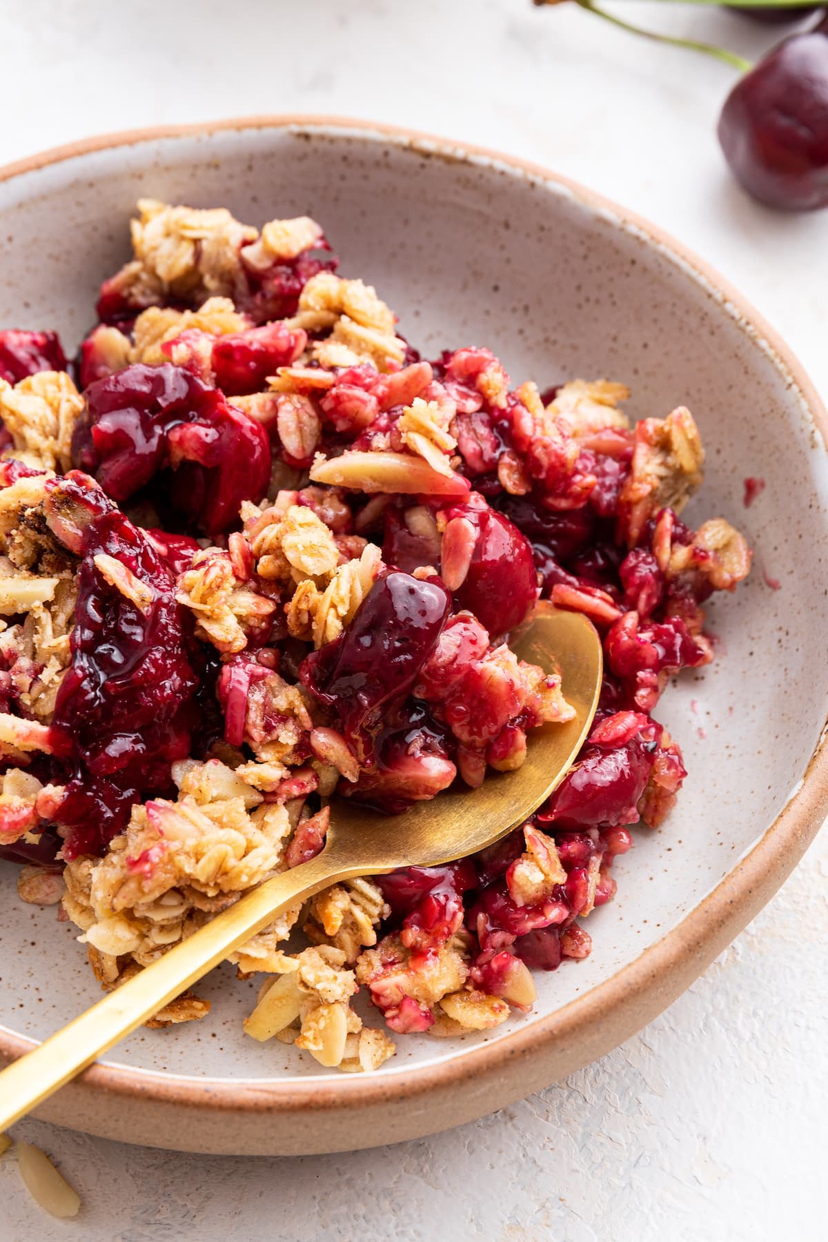 Cherry crisp on a small plate with a golden metal spoon.