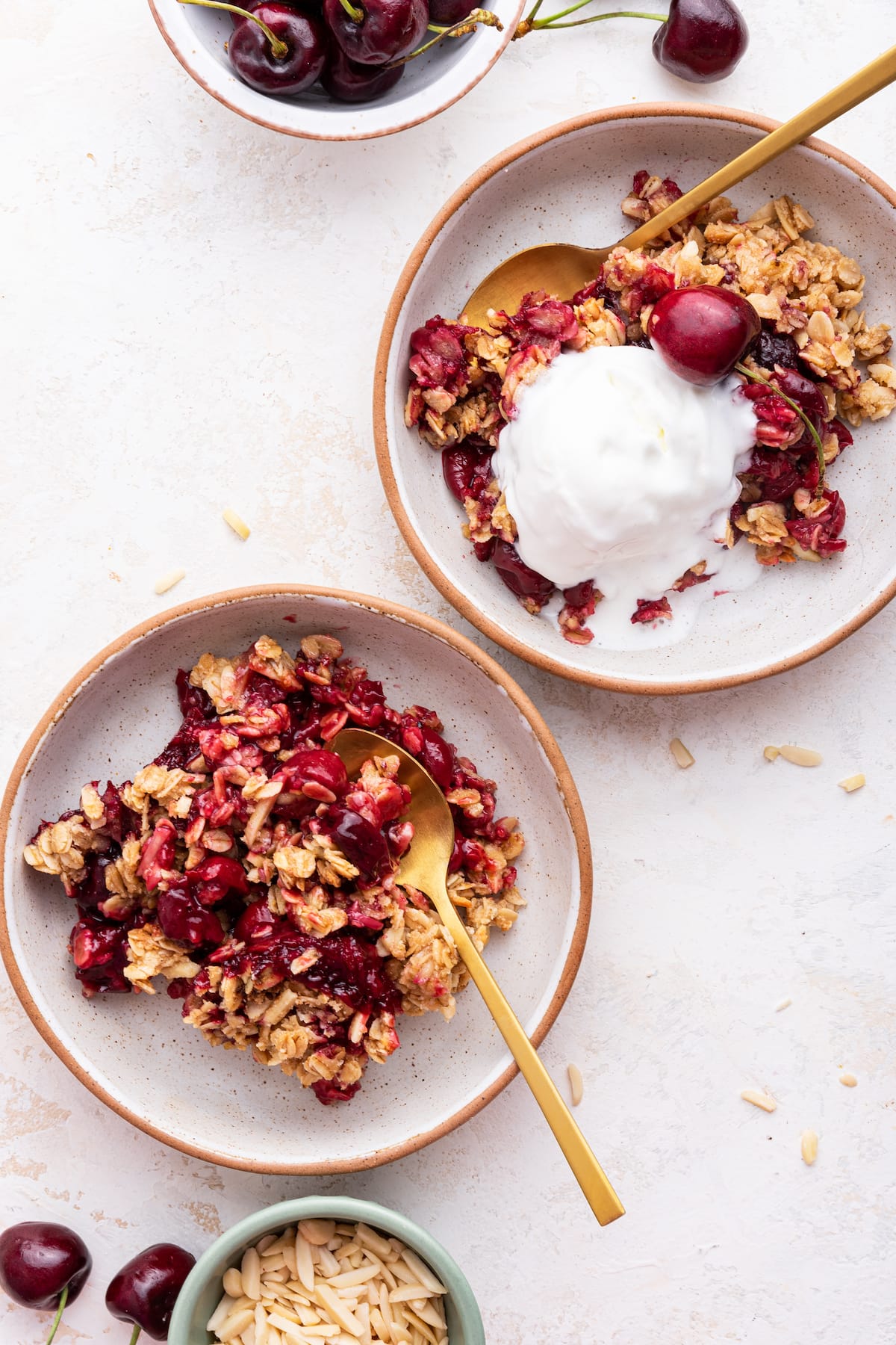 Two small plates with servings of cherry crisp. One plate has a scoop of ice cream with a whole cherry on top, while the other plate contains only the cherry crisp.