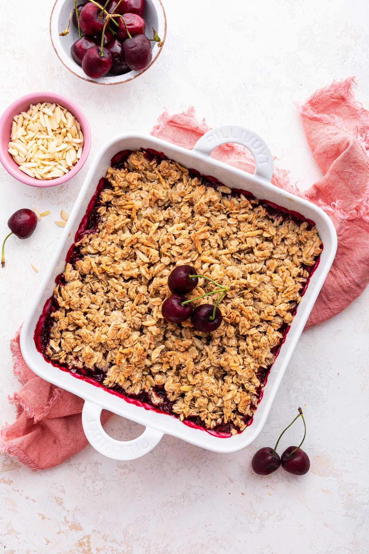 Cherry crisp in a square baking dish with three whole cherries in the center.