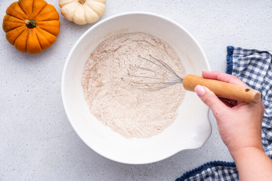A woman's hand uses a whisk to mix the dry ingredients for the healthy pumpkin bread.