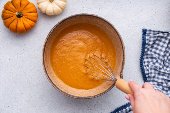 A woman's hand uses a whisk to mix the wet ingredients for the healthy pumpkin bread in a large bowl.