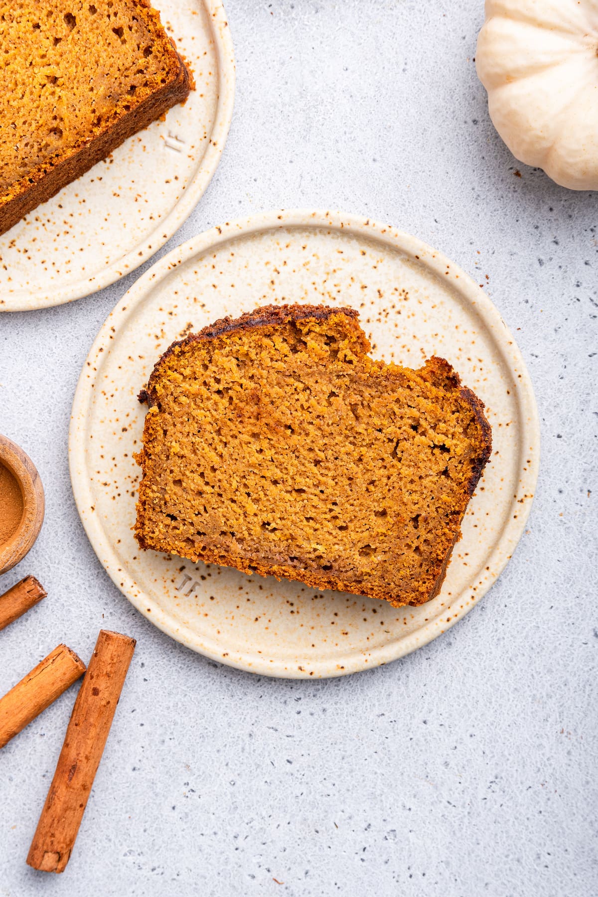 A slice of healthy pumpkin bread on a small plate with a small bite taken out of it.