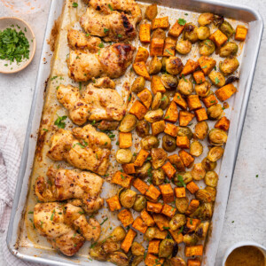 A large sheet pan with honey mustard chicken and roasted sweet potatoes and brussels sprouts.
