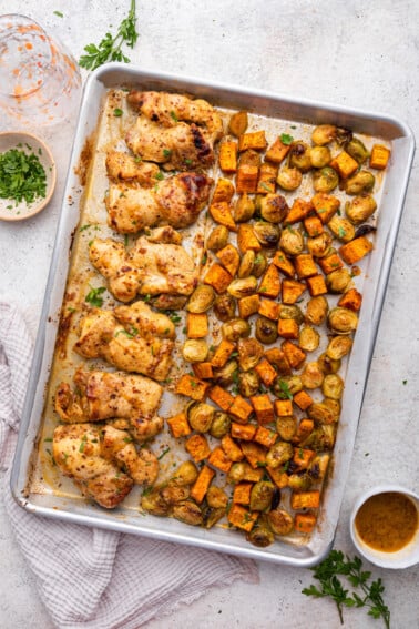 A large sheet pan with honey mustard chicken and roasted sweet potatoes and brussels sprouts.