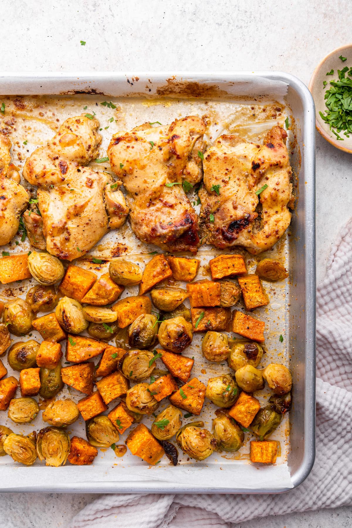 A large sheet pan with honey mustard chicken and roasted sweet potatoes and brussels sprouts.