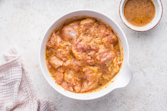 Raw chicken marinating in a large bowl with a honey mustard marinade.