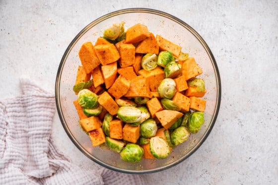 Cubed sweet potato and halved brussels sprouts in a large glass bowl.