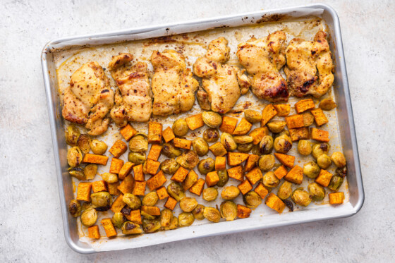 A large sheet pan with honey mustard chicken and roasted sweet potatoes and brussels sprouts.