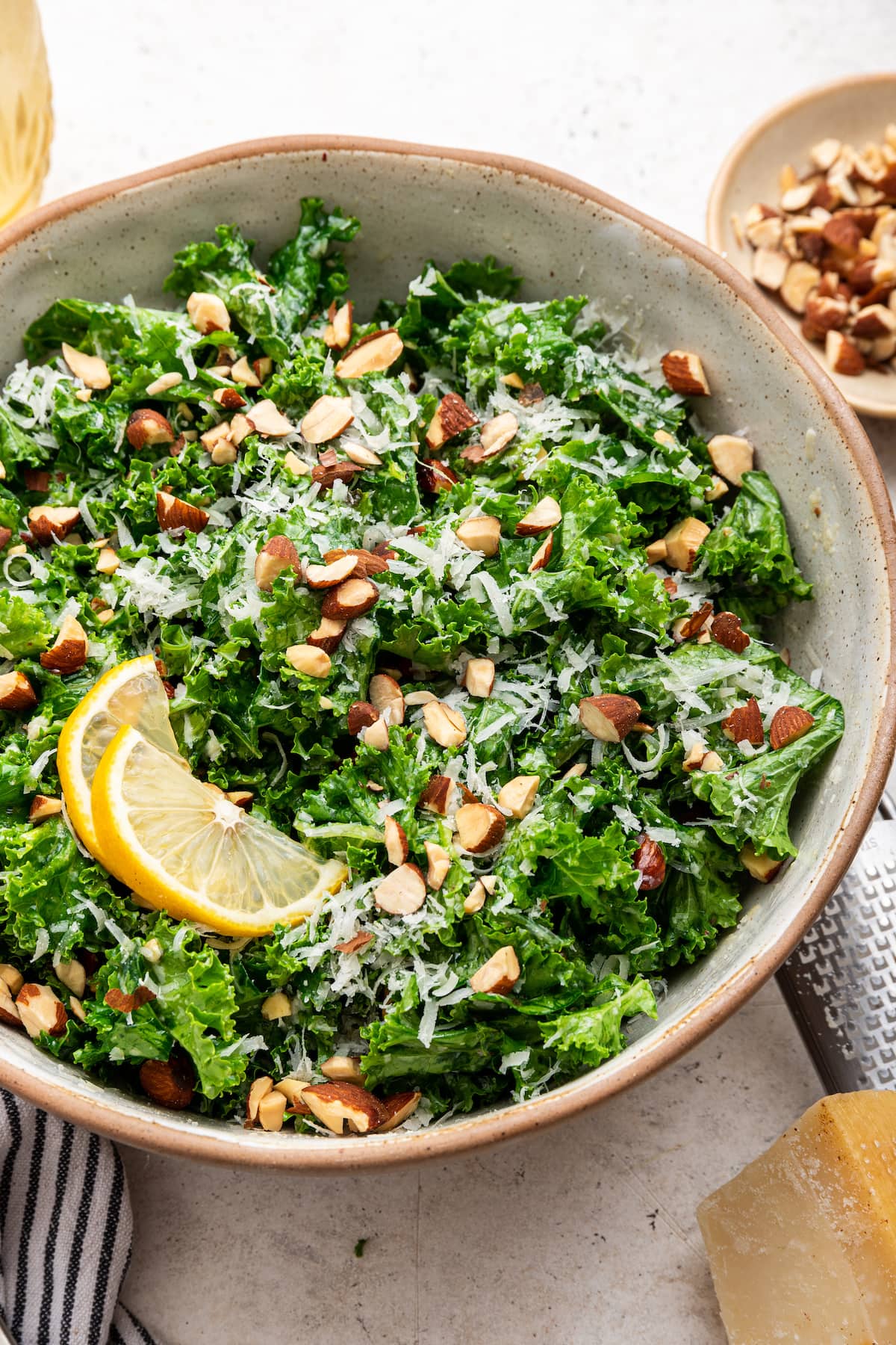 Kale salad in a serving bowl topped with almonds, parmesan cheese and lemon slices.