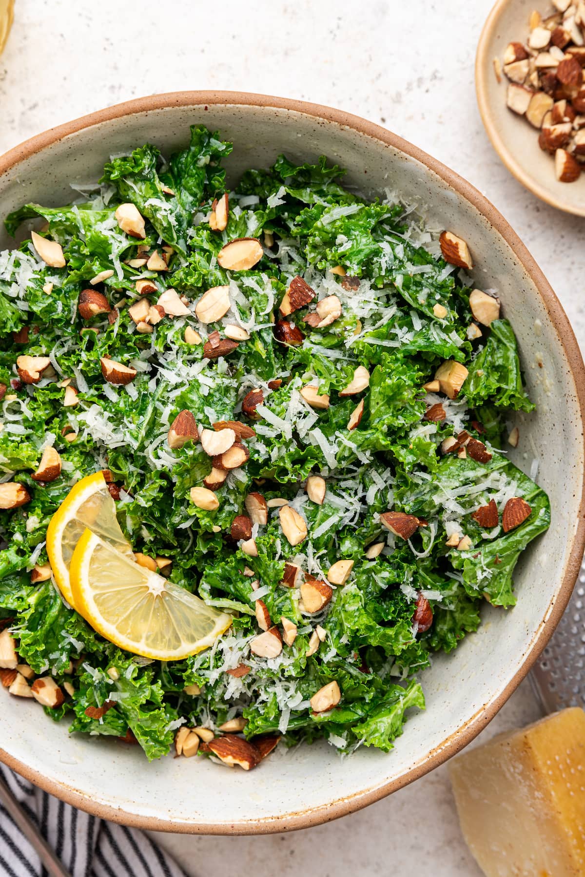 Kale salad in a serving bowl topped with almonds, parmesan cheese and lemon slices.