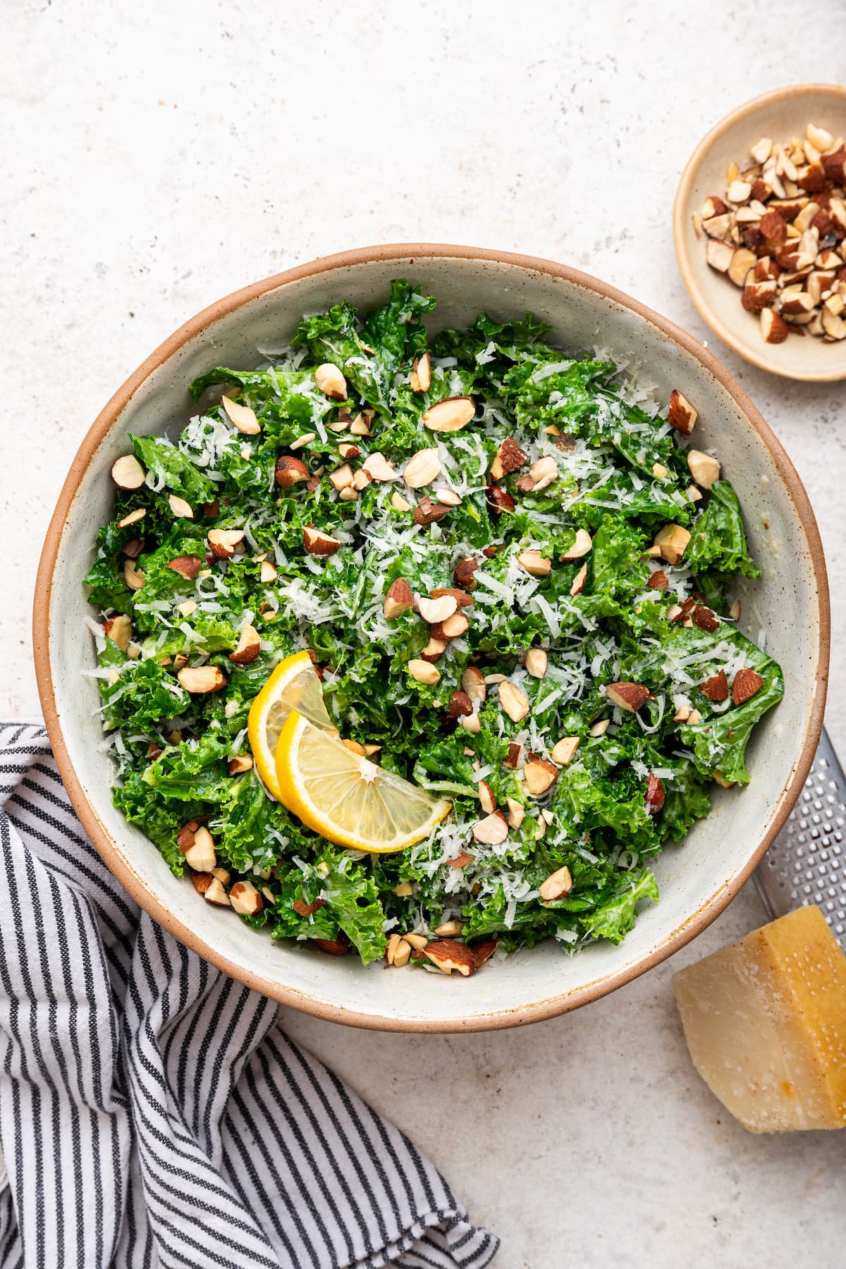 Kale salad in a serving bowl topped with almonds, parmesan cheese and lemon slices.