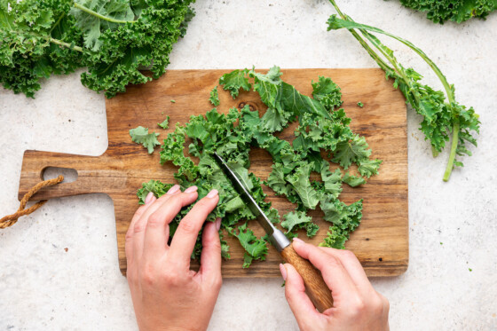 Woman's hands chopping kale on a wooden cutting board.