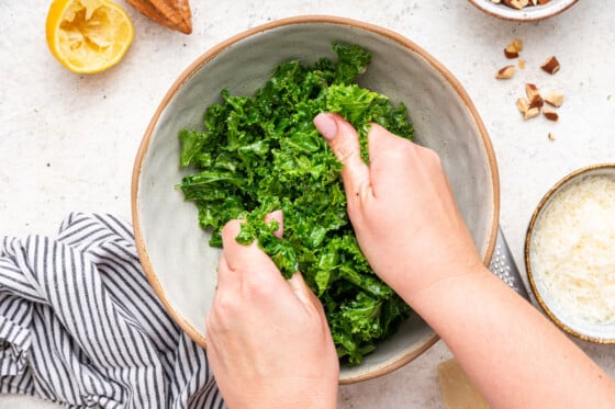 Woman's hands massaging the kale leaves with the lemon dressing in the serving bowl.