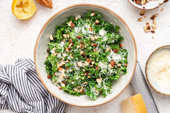 Kale salad in a serving bowl topped with almonds, parmesan cheese and lemon slices.