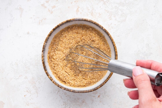 A woman's hand uses a metal whisk to mix ground flaxseed with water.