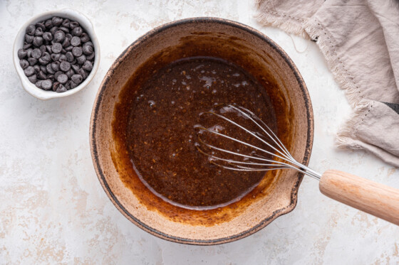 A metal whisk in a mixing bowl of the wet ingredients for the lactation cookies.