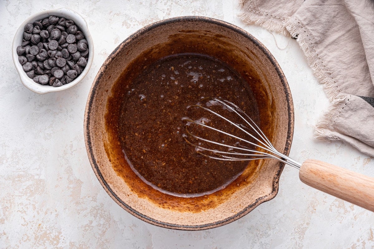 A metal whisk in a mixing bowl of the wet ingredients for the lactation cookies.