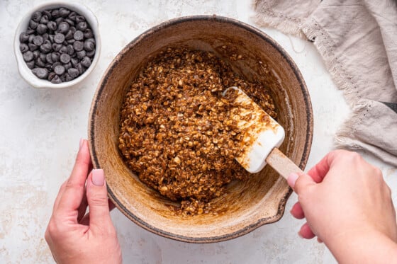 A woman's hand uses a silicone spatula to fold the wet and dry ingredients together for the lactation cookies.