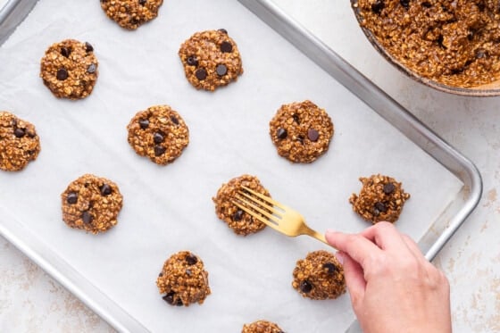 A woman's hand uses a fork to press down and form the lactation cookies on a baking sheet.