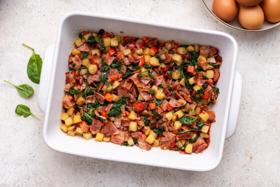 Potatoes, bell pepper, turkey bacon, and spinach in a large square baking dish.