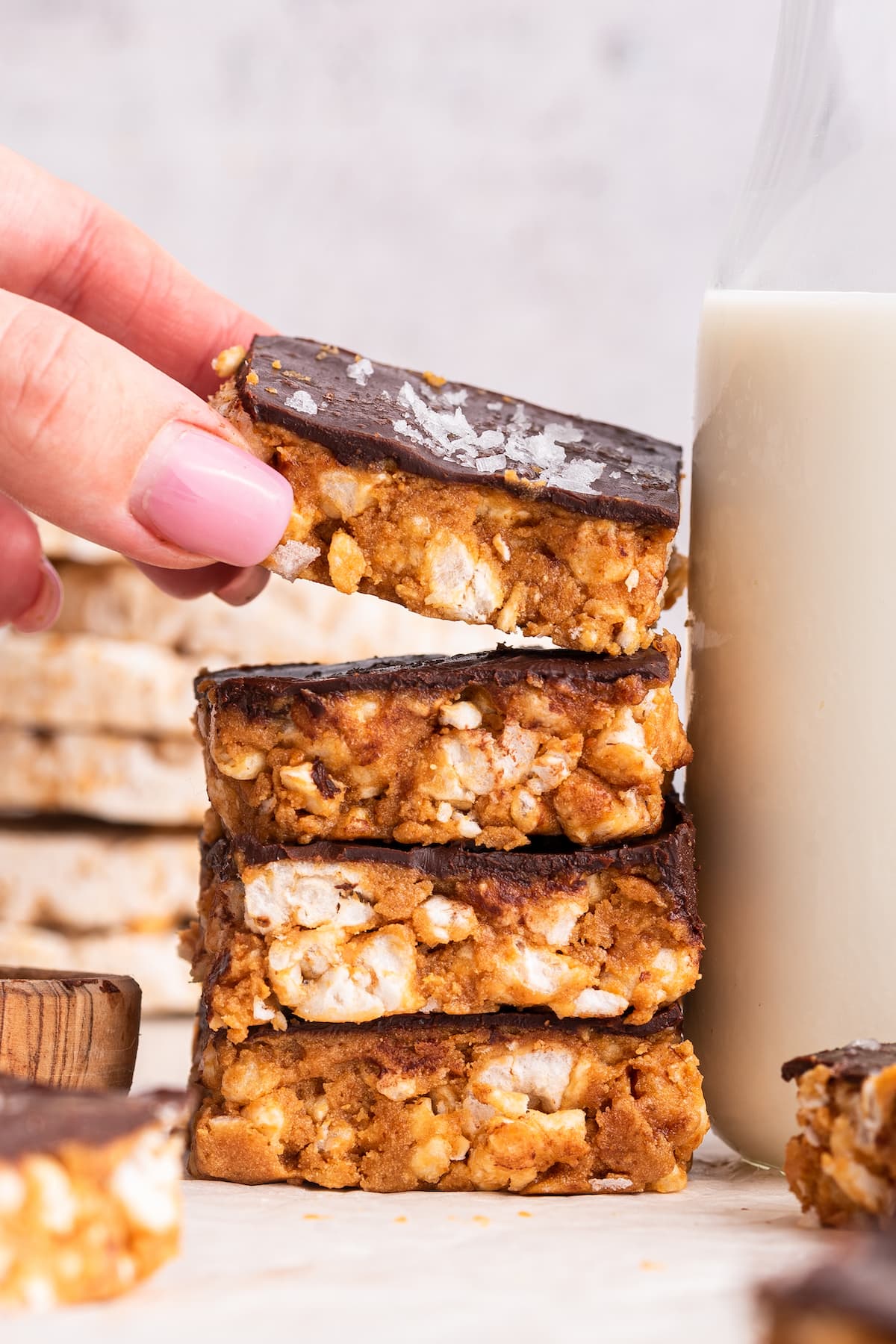 Four no bake peanut butter crunch bars stacked on one another with a woman's hand taking the top one.