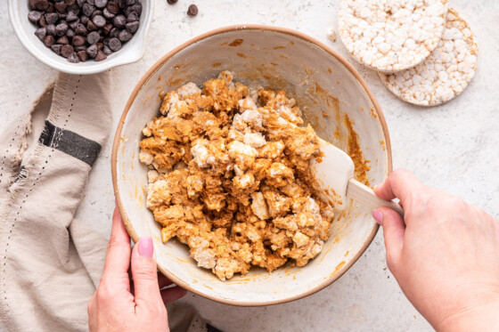 A womans hand using a silicone spatula to mix all the ingredients for the no bake peanut butter crunch bars in a large mixing bowl.