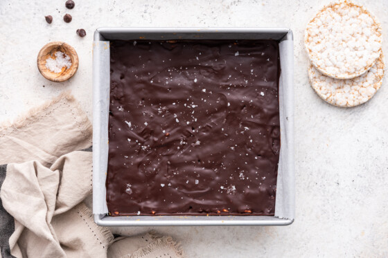 No bake peanut butter crunch bars with a chocolate coating and topped with flaky sea salt in a square baking dish.