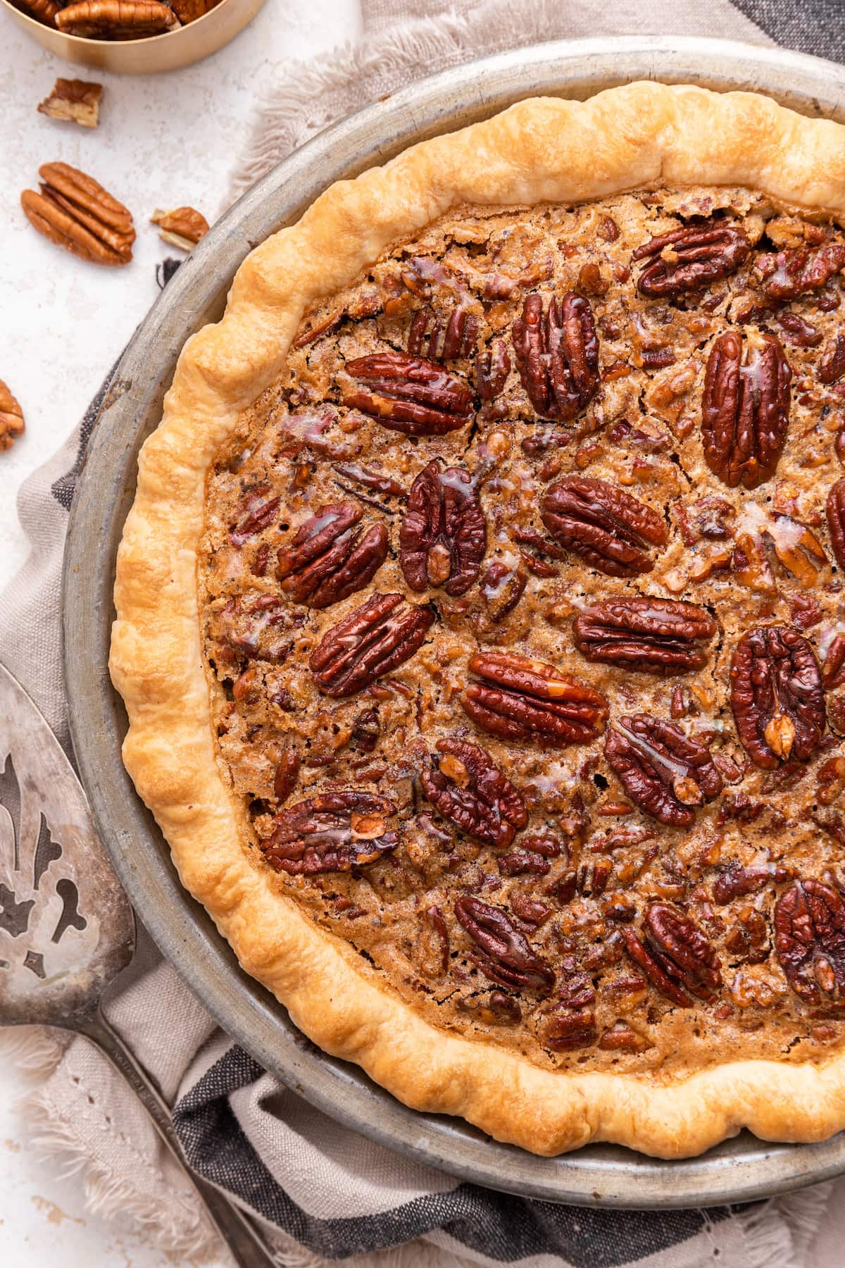 Uncut pecan pie in a pie dish with pecan halves on top.