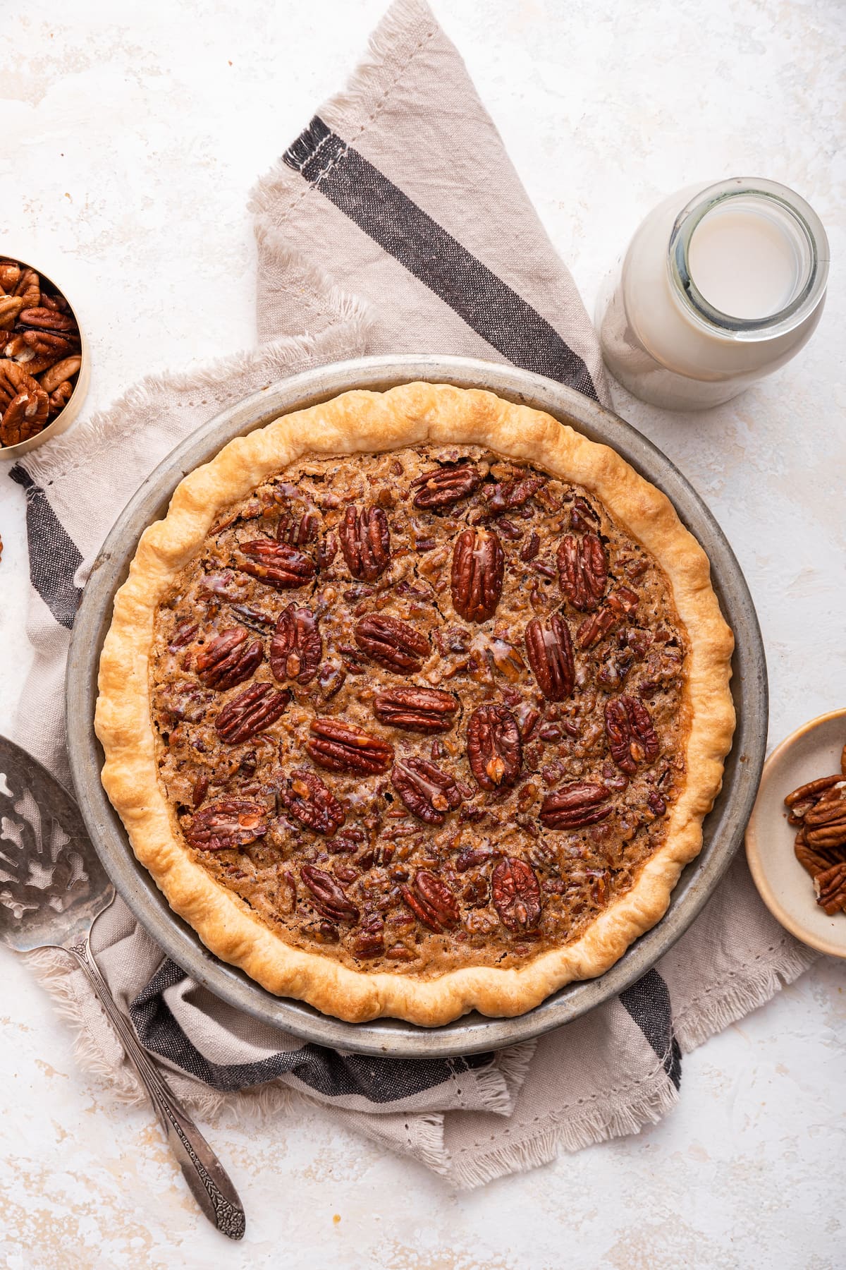 Uncut pecan pie in a pie dish with pecan halves on top.