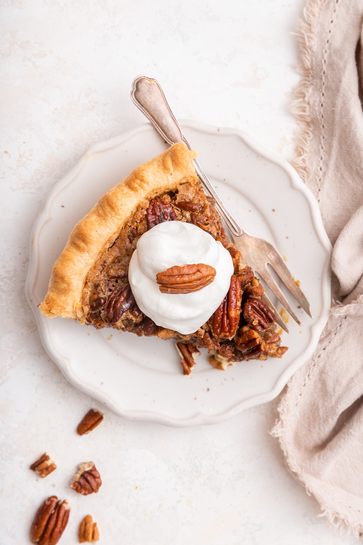 A slice of pecan pie topped with whipped cream and a pecan half served on a plate with a fork.
