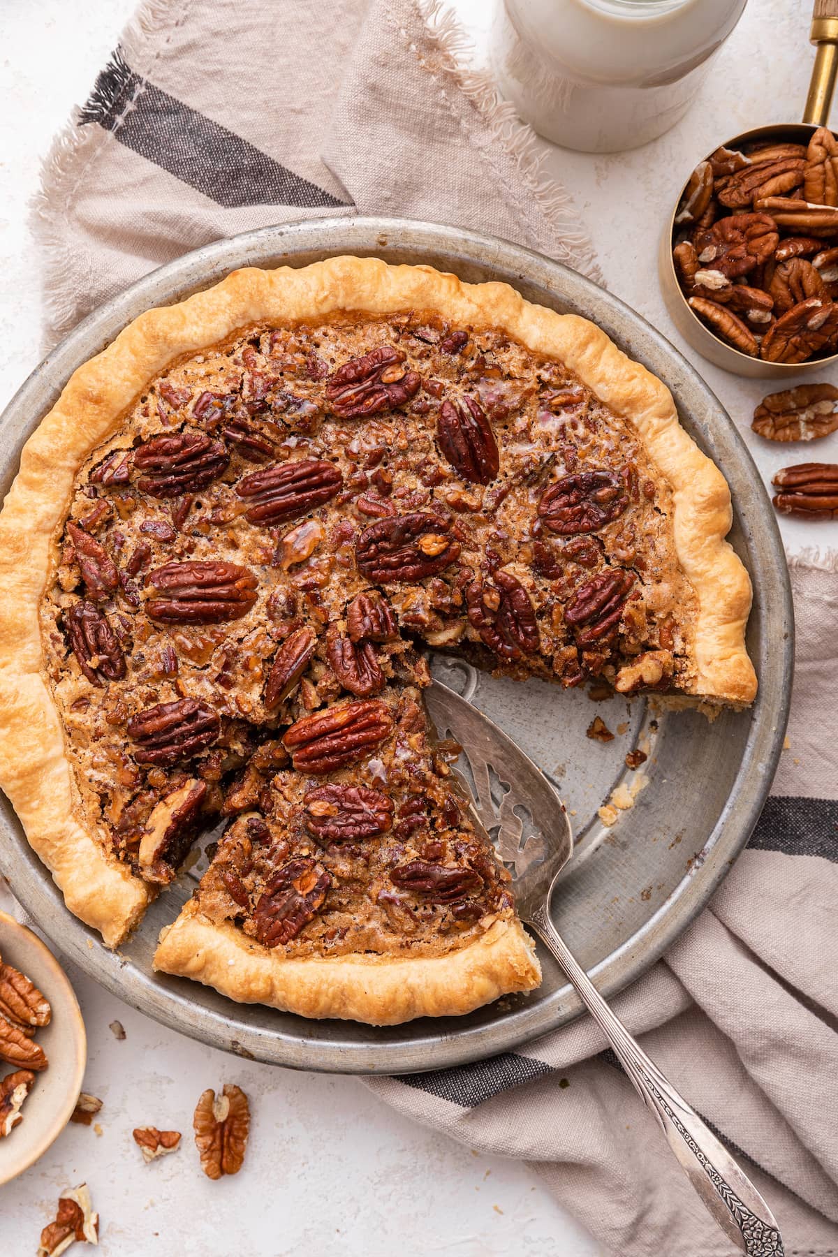 Pecan pie in a pie dish with pecan halves on top. One piece has been removed and a serving utensil is in the pie dish.