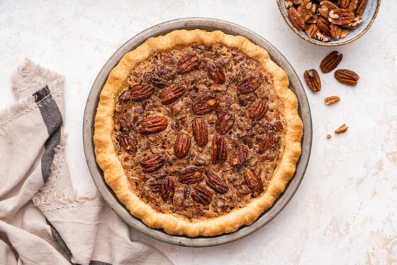 Uncut pecan pie in a pie dish with pecan halves on top.