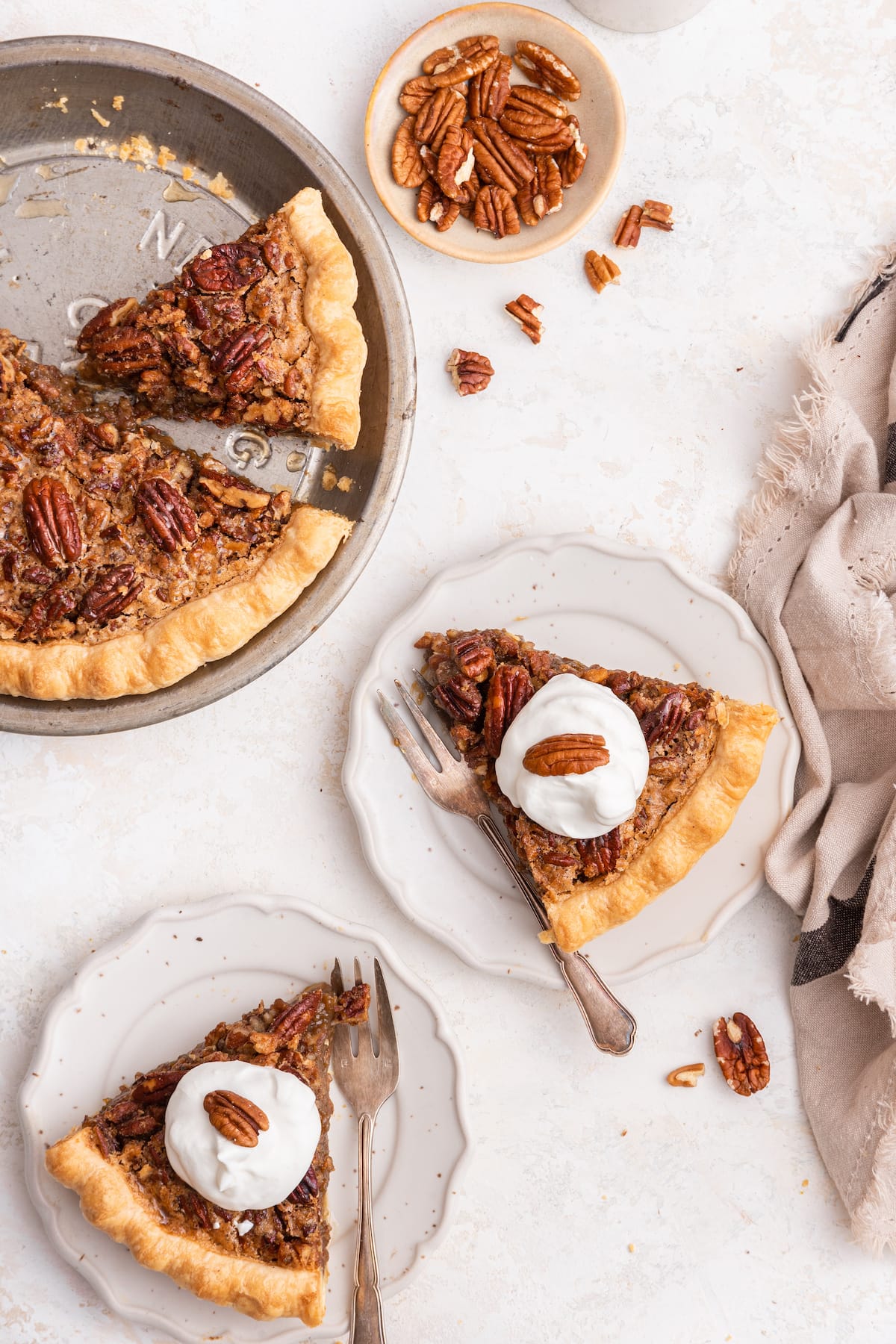 Two slices of pecan pie topped with whipped cream and pecan halves served on plates. The full pecan pie is next to the slices.