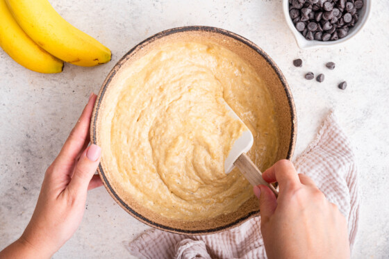 A woman using a silicone spatula to mix the wet and dry ingredients to create the batter for the protein banana bread.