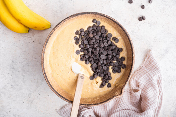 Chocolate chips added to a large bowl of protein banana bread batter with a silicone spatula.