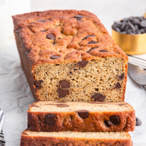A loaf of protein banana bread with chocolate chips near two slices that are leaning on one another.
