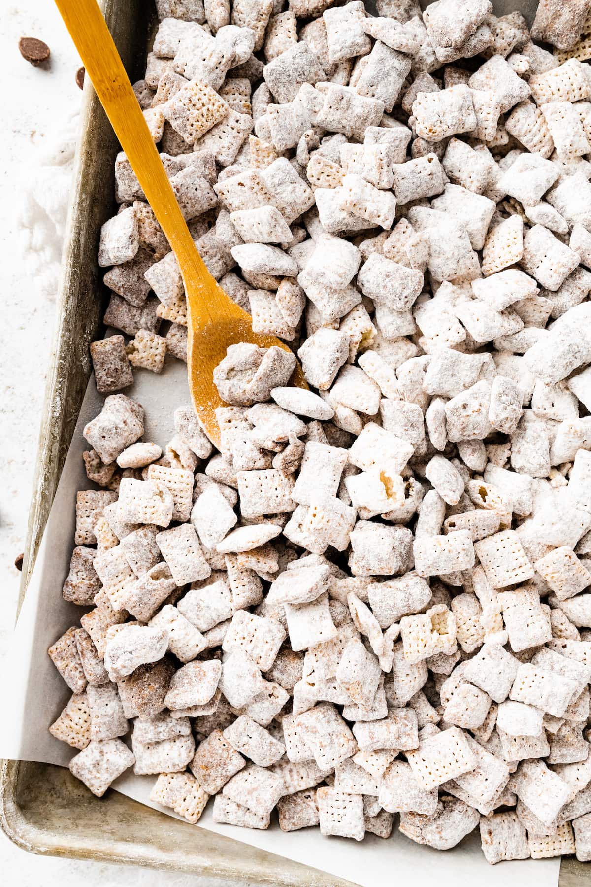 Puppy chow on a baking tray with a small wooden spoon.