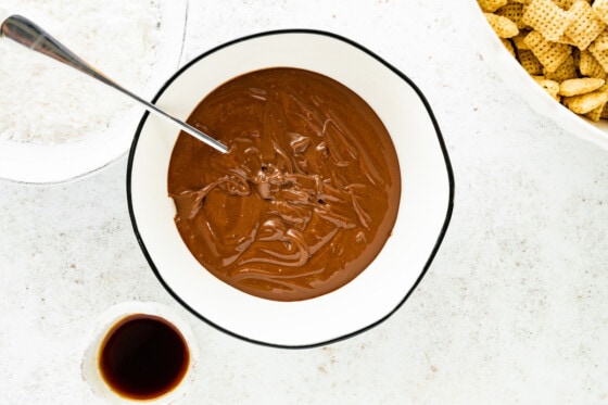 Melted chocolate in a small bowl with a spoon that will be used for puppy chow.