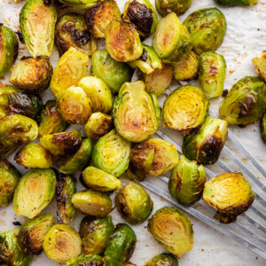 Roasted brussels sprouts on parchment paper on a baking tray with a spatula.